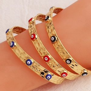 Dettaglio di bracciali a polsino in oro 18K con ciondoli a forma di occhio smaltati