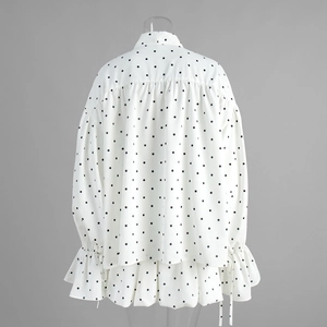 Detailed view of white polka dot blouse featuring ruffle hem and ruched back design
