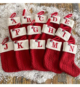 Close-up of red cable knit Christmas stockings with ivory letter embroidery and snow