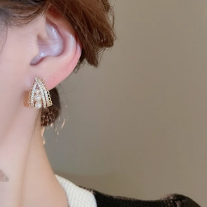 Detailed close-up of gold layered hoop earrings with three pearls and small crystals
