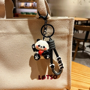 Cute UV plated panda keychain holding a red apple hanging on a canvas bag strap