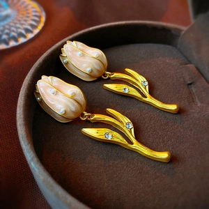 Gros plan de boucles d'oreilles tulipes en émail pêche et perles dans un écrin brun