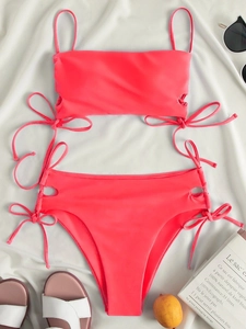 Neon pink bikini set with side cut-out drawstring bows displayed on a white fabric background