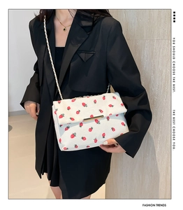Detail of white strawberry print crossbody bag with gold lock and textured fabric