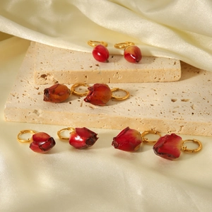 Artistic detail of red rose earrings with gold rings on beige stone and silk background