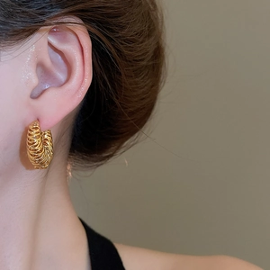 Gros plan de boucles d'oreilles créoles torsadées dorées portées par un mannequin chic