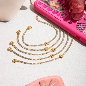 Close-up of gold tennis bracelets with crystal A-E balloon letter pendants on white stone