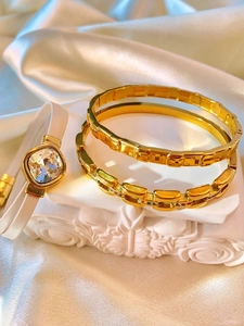 Detail of gold metal bracelets and white leather rhinestone wristband on white satin