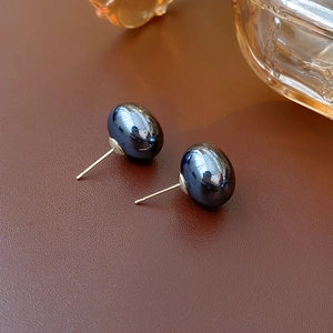 Macro detail of dark blue oval pearl earrings with gold-tone studs on leather