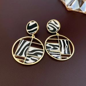 Détail macro de boucles d'oreilles géométriques dorées avec motif zébré noir et blanc