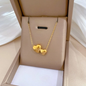Polished gold double heart pendant necklace displayed in an elegant jewelry box