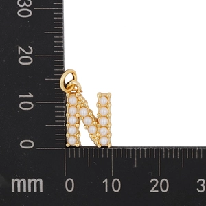 Macro shot of gold letter N necklace pendant with pearls next to a metric ruler scale