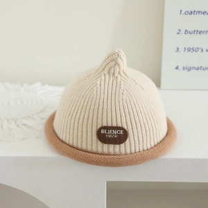 Detail of beige ribbed knit baby beanie with rolled brim and brown logo patch accent