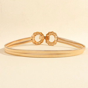 Detail of gold elastic spring belt featuring decorative floral leaf buckle on beige background