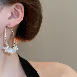 Macro view of a silver hoop earring featuring white acrylic flowers and metal beads