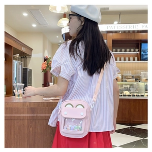 Close-up of pink bear-eared crossbody bag with clear window showing badges worn by model