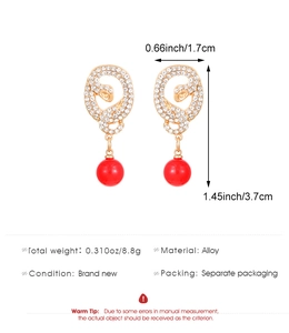 Detail view of gold-tone snake earrings with cubic zirconia and red bead drops