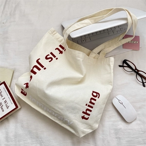 Sac fourre-tout en toile crème avec slogan rouge parmi des accessoires de bureau variés