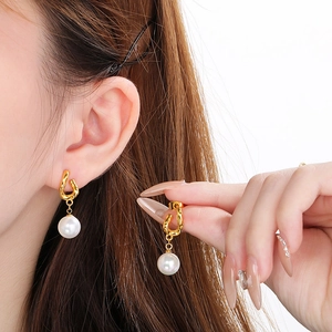 Close-up of golden bow-shaped pearl earrings worn by a model against white background