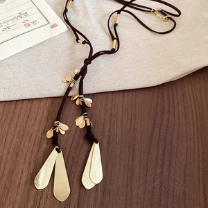 Detailed view of a long brown woven necklace with golden metal water drop tassel pendants