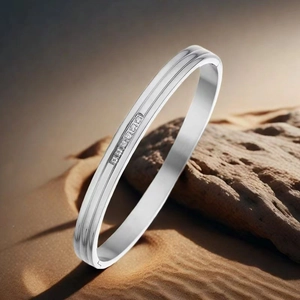 Close-up of silver stainless steel bangle with single row of zircons on sand background