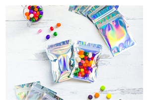Iridescent laser zip lock bags filled with colorful candies on white wood background