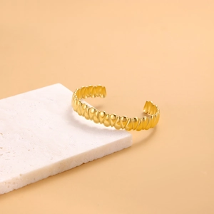Detailed view of an open golden cuff bracelet with wavy texture on a stone base
