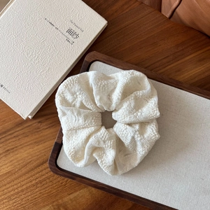 Detailed macro view of an oversized white lace scrunchie with floral embroidery on wood