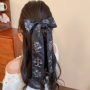 Detail of black satin bow hair tie with white floral print on a half-up ponytail