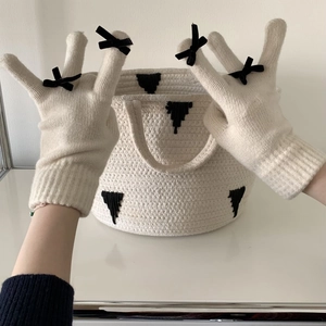 Detail of cream knit gloves with black bow accent and matching storage basket