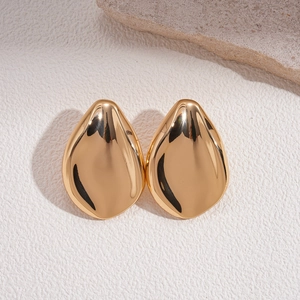 Polished gold irregular leaf stud earrings on minimalist stone decor background