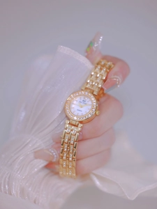 Close-up of luxury gold ladies watch with crystal encrusted bezel and white dial on wrist
