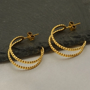 Minimalist double-hoop geometric gold earrings with beaded texture on a stone background
