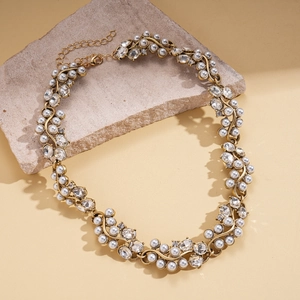 Détail d'un collier doré vintage avec perles blanches et cristaux sur fond de pierre
