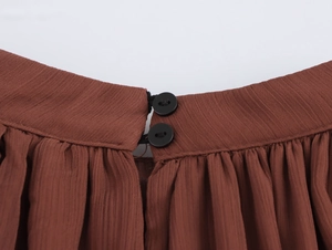 Dettaglio dello scollo in chiffon plissettato marrone con due bottoni neri su bianco