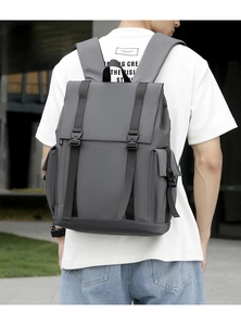 Rear view of model wearing a grey casual backpack with buckle flap in urban setting