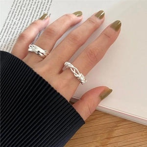 Close-up of minimalist 925 silver knotted and twisted rings on hand with magazine background