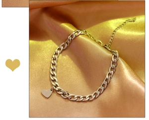 Detailed view of silver heart pendant on cuban link chain over golden satin fabric