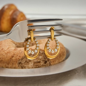 Elegant 18K gold plated stainless steel pearl earrings hanging on a fork in lifestyle scene