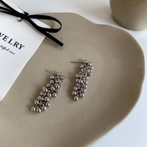 Close-up of silver beaded tassel earrings with high-polish metallic finish on ceramic tray