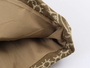 Détail de la broderie ethnique beige sur tissu marron avec doublure lisse