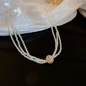 Détail d'un collier de perles à trois rangs avec un pendentif sphérique doré serti de diamants