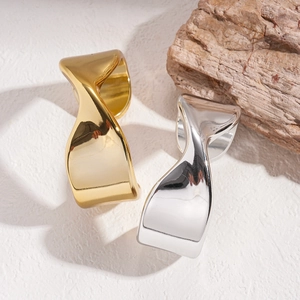 Minimalist twisted wide rings in polished gold and silver finish on white textured stone
