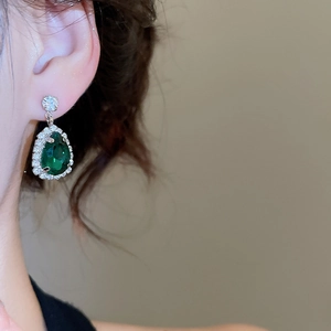 Close-up of teardrop green gemstone earring with silver zircon paving on a model