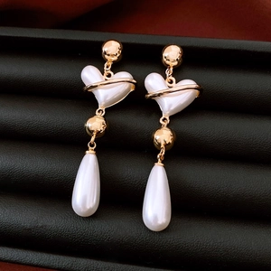 Macro detail of vintage heart and teardrop pearl drop earrings with golden accents