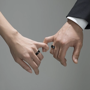 Minimalist black tungsten steel couple rings worn by male and female models on grey background
