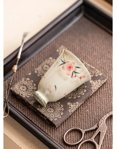 Detailed view of a hand-painted ceramic peach blossom tea cup on a woven tray