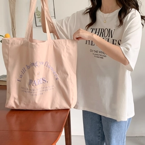 Detail of light pink canvas tote bag featuring purple embroidery and floral text design