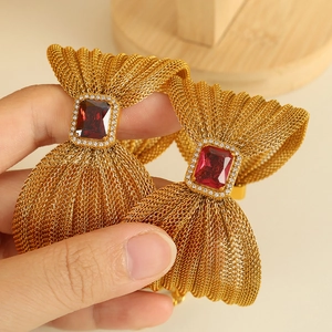 Golden mesh bow bracelet with red gemstone and zircon accents on a wooden stand