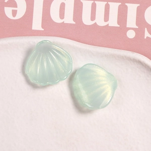 Detalle de dos dijes de resina verde claro iridiscente en forma de concha para joyería DIY